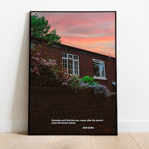 May include: A framed print with a photograph of a brick building with a window and a pink and orange sunset sky. The quote "Someday we'll find the love, cause after the storm's when the flowers bloom. Kali Uchis" is printed below the image.