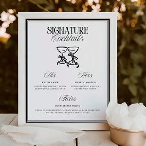 May include: A white framed sign with black text and illustrations of two glasses. The sign reads "SIGNATURE Cocktails" and lists three cocktails: "Whiskey Sour", "Espresso Martini", and "Huckleberry Mojito".
