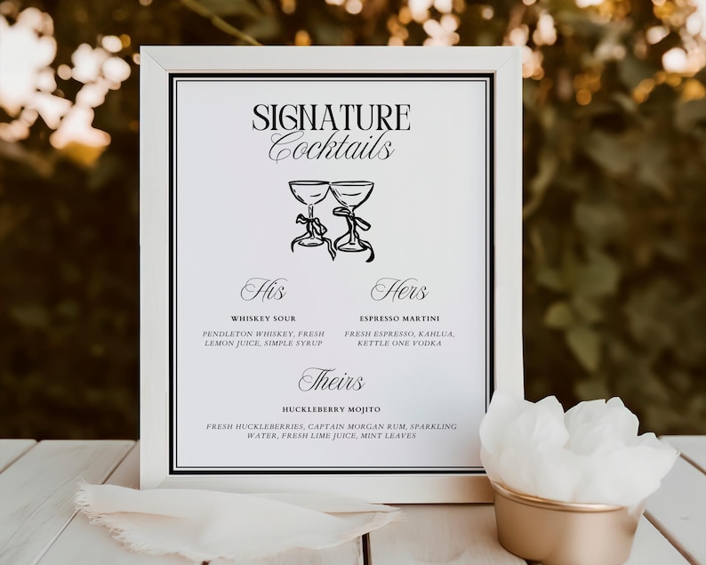 May include: A white framed sign with black text and illustrations of two glasses. The sign reads "SIGNATURE Cocktails" and lists three cocktails: "Whiskey Sour", "Espresso Martini", and "Huckleberry Mojito".
