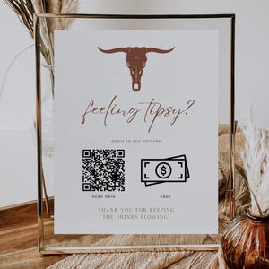 May include: A framed sign with a brown bull skull graphic and the text "feeling tipsy?" It includes a QR code and a cash icon, with the words "scan here" and "cash" below. The sign reads "THANK YOU FOR KEEPING THE DRINKS FLOWING!"