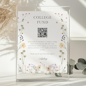 May include: A white card with a floral design and the text "COLLEGE FUND" printed on it. A QR code is also printed on the card. The text below the QR code reads: "If you wish to contribute to Audrey's college fund, please scan the QR code. Your contribution allows Audrey to continue her journey and focus on her studies in business at USC. Thank you for your love and support. Audrey."