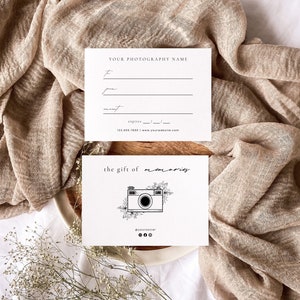 May include: A white gift certificate with black text that reads "the gift of memories". A black and white illustration of a camera with flowers is above the text. The text "@yoursocial" is below the illustration.
