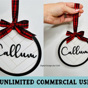May include: A round Christmas ornament with a black frame, the name "Callum" in black script, and a white herringbone pattern background. It has a red and black plaid ribbon for hanging.
