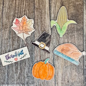 May include: A set of six wooden Thanksgiving-themed decorations. The decorations include a pilgrim hat, a cornucopia, a turkey, a pumpkin, a leaf, and a sign that says "thankful".