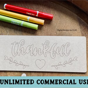 May include: A wooden sign with the word "thankful" written in a cursive font. The sign also has a heart and two branches with leaves. The sign is on a wooden surface with three markers.