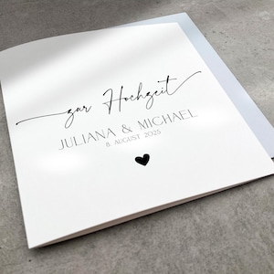 Könnte beinhalten: Eine weiße Karte mit schwarzem Text, auf der "zur Hochzeit" Juliana & Michael 8. August 2025 steht. Unter dem Text befindet sich ein kleines schwarzes Herz.