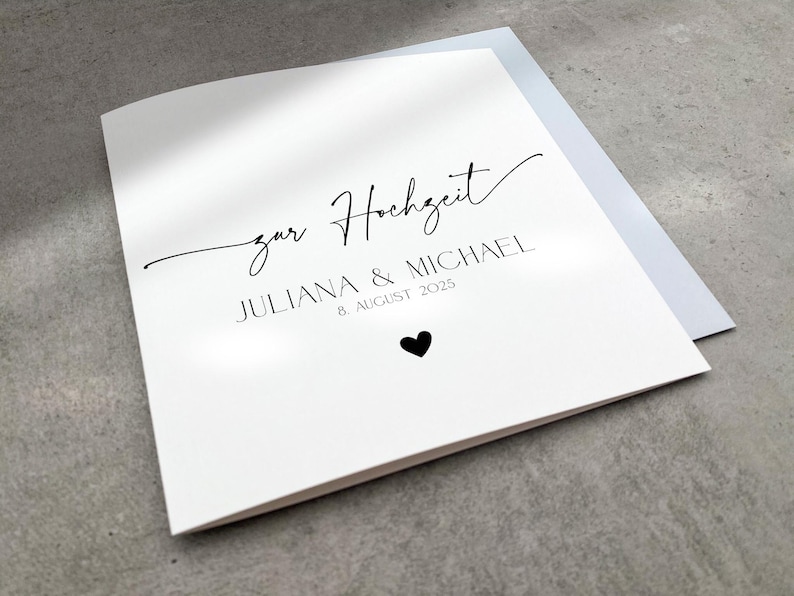 Könnte beinhalten: Eine weiße Karte mit schwarzem Text, auf der "zur Hochzeit" Juliana & Michael 8. August 2025 steht. Unter dem Text befindet sich ein kleines schwarzes Herz.