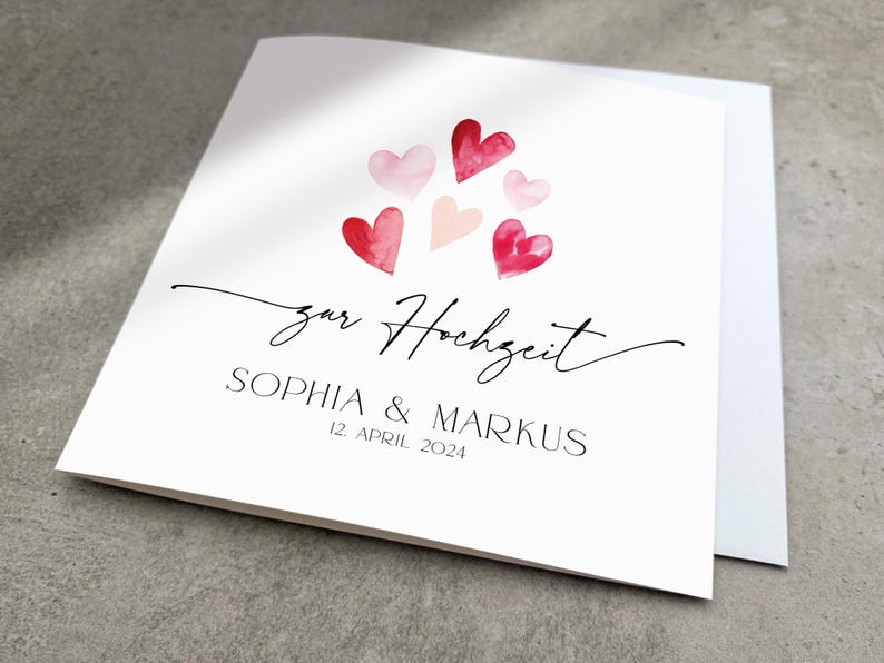 May include: A white card with a watercolor illustration of pink and red hearts. The text "zur Hochzeit" is written in black cursive script. Below the hearts, the text "Sophia & Markus" is written in black, followed by the date "12. April 2024".