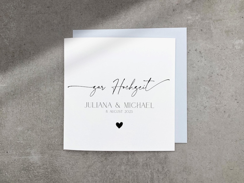 May include: A white card with black text that says "zur Hochzeit" Juliana & Michael 8 August 2025. A small black heart is below the date.