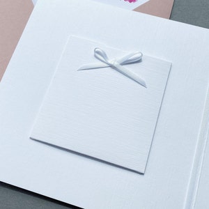 May include: A white card with a white ribbon tied in a bow on top. The card is blank and ready for a message.