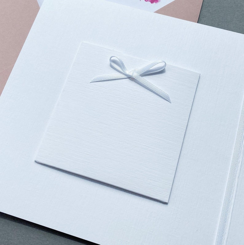 May include: A white card with a white ribbon tied in a bow on top. The card is blank and ready for a message.