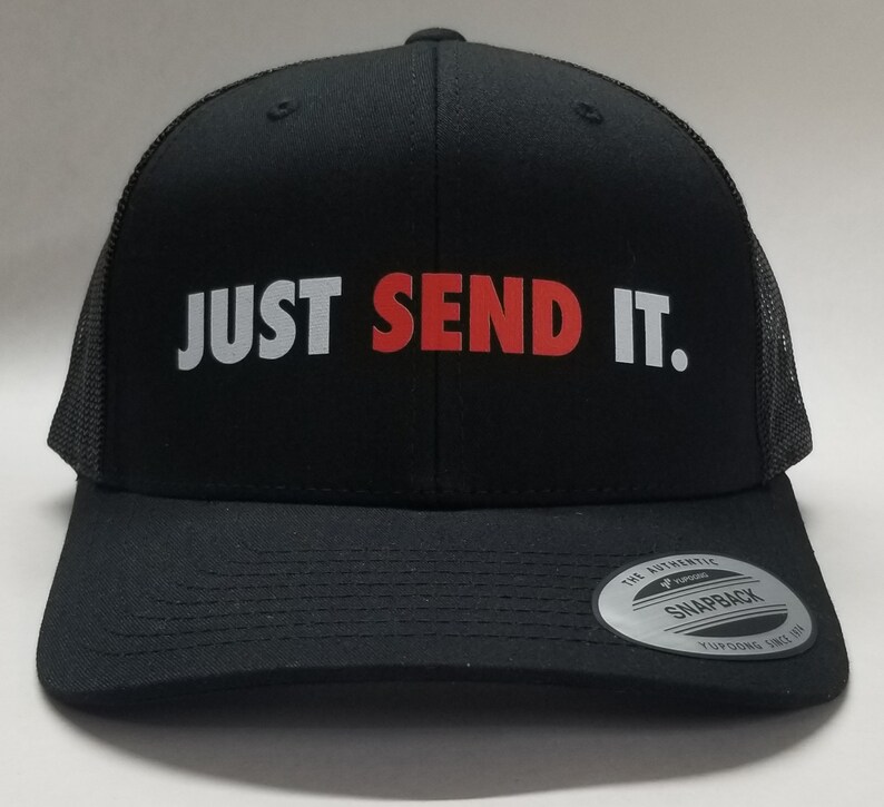 K&ouml;nnte beinhalten: Schwarze Trucker-Kappe mit wei&szlig;em Netzr&uuml;cken. Die Kappe hat die Worte "JUST SEND IT." in Wei&szlig; und Rot auf der Vorderseite gestickt.
