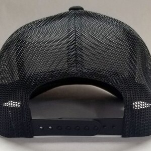 K&ouml;nnte beinhalten: Schwarze Mesh-Trucker-Kappe mit schwarzem verstellbarem Riemen und einer schwarzen Kunststoffschnalle.