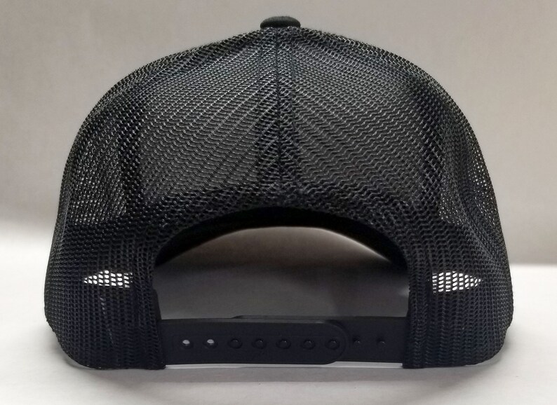 K&ouml;nnte beinhalten: Schwarze Mesh-Trucker-Kappe mit schwarzem verstellbarem Riemen und einer schwarzen Kunststoffschnalle.