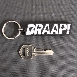 May include: A black keychain with the word "BRAAAP!" in white lettering and a silver key with the number "12533" printed on it. The keychain has a silver key ring attached.