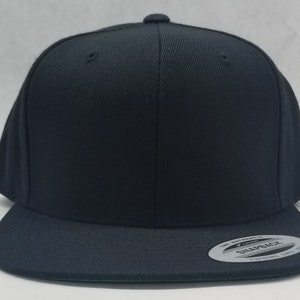 May include: A black flat brimmed baseball cap with a black undervisor. The cap has a black snap closure and a white label on the back that says "The Authentic Snapback Yupoong, Since 1974."