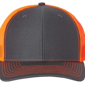 May include: A charcoal gray and orange trucker hat with a mesh back. The hat has a curved brim and a contrasting orange stitching detail.