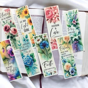 May include: A collection of eight rectangular paper bookmarks featuring watercolor floral illustrations and religious text. Each bookmark displays unique botanical designs, including roses, sunflowers, and daisies, paired with inspirational quotes.