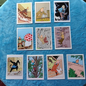 Könnte beinhalten: Eine Sammlung von zehn Vintage-Comic-Sammelkarten mit farbenfrohen Illustrationen einer Zeichentrickfigur und ihres Hundes in verschiedenen Action-Szenen. Die Karten sind auf einer blauen Oberfläche angeordnet.