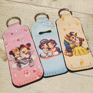 May include: Three keychains with different Disney couples. The first keychain is pink with Mickey and Minnie Mouse. The second keychain is blue with Aladdin and Jasmine. The third keychain is beige with Belle and the Beast.