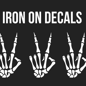 Puede incluir: Calcomanías para planchar con tres manos de esqueleto blancas haciendo el signo de la paz sobre un fondo negro. El texto "IRON ON DECALS" se muestra en blanco en la parte superior de la imagen.