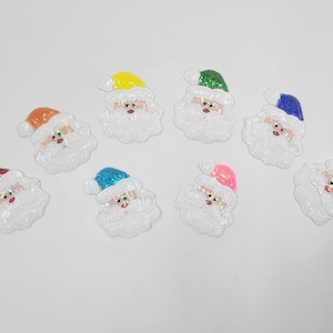 Op de afbeelding: Een verzameling van acht Santa Claus gezicht patches. Elke patch heeft een witte, met pailletten bezette baard en gezicht, met kleurrijke mutsen in rood, oranje, geel, groen, blauw, roze en paars. Voor knutselen en kerstversieringen.