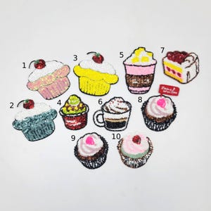 Könnte beinhalten: Eine Sammlung von zehn Cupcake- und Dessert-Patches mit Pailletten. Die Patches weisen verschiedene Farben auf, darunter Rosa, Gelb, Grün und Braun. Jeder Patch hat ein einzigartiges Design, einige mit Kirschen und Schlagsahne.