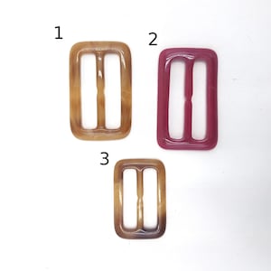 Puede incluir: Tres cierres de hebilla de plástico. Uno es marrón, uno es rosa y uno es marrón moteado. Las hebillas están numeradas 1, 2 y 3.