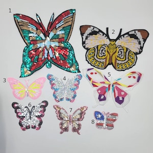 May include: A collection of eight butterfly patches in various colors and designs. The patches are embellished with sequins and embroidery, featuring shades of red, green, pink, blue, white, and gold. These decorative patches are suitable for clothing and craft projects.