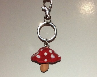May include: A red and white mushroom keychain with a silver key ring and clasp.