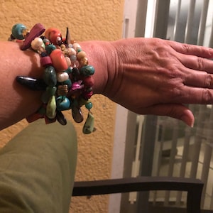 May include: A stack of colorful bracelets with turquoise, coral, and other stones. The bracelets are on a person's wrist.