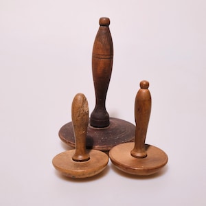Może przedstawiać: Trzy antyczne drewniane przedmioty w odcieniach ciemnego i jasnego brązu. Centralny przedmiot jest wysoki i cylindryczny, podczas gdy pozostałe dwa są krótsze z okrągłą podstawą. Przedmioty wydają się być ręcznie robione.
