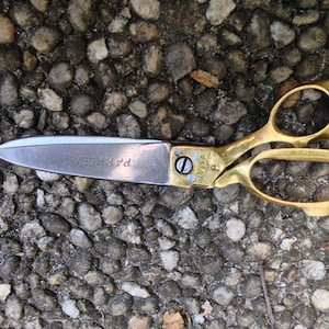 Puede incluir: Un par de tijeras de tela doradas con una cuchilla plateada. La cuchilla está marcada con "PARVEEN" y "MADE IN INDIA".
