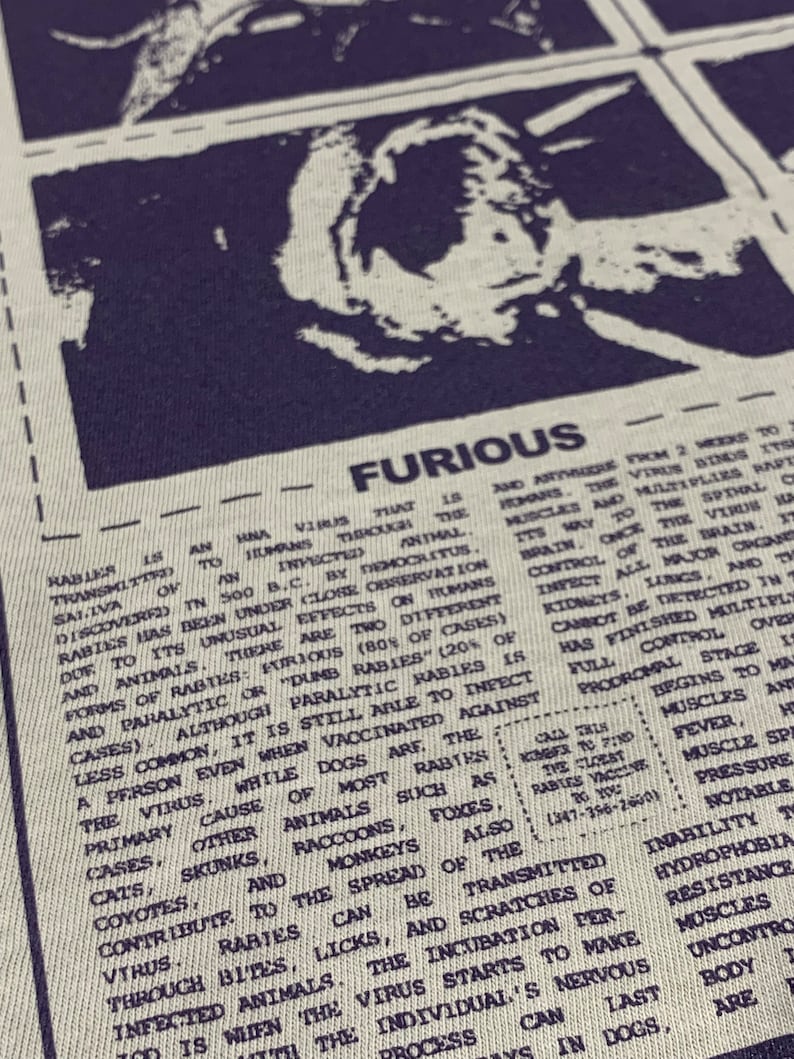 May include: A close-up of a black and white printed graphic t-shirt with the word "FURIOUS" in bold letters. The text describes rabies, a viral disease that can be transmitted to humans through bites from infected animals. The text also includes a phone number for the closest rabies vaccine.