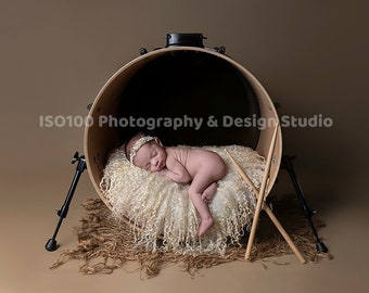 May include: A newborn baby sleeping inside a brown bass drum with a white fluffy blanket and two wooden drumsticks on the floor. The text "ISO100 Photography & Design Studio" is visible on the drum.
