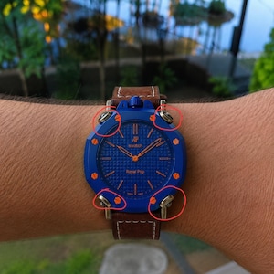 May include: A blue AP Royal Pop watch with a brown leather strap. The watch face has a textured pattern and the text "AP Swatch Royal Pop". The watch is on a wrist.