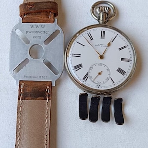 May include: A classic pocket watch with a white dial, black Roman numerals, and a seconds subdial. It is shown with a brown leather strap and a metal adapter with the text "www.pwconverter.com" and "Patent no: 112/21". Four black watch cushions are also present.