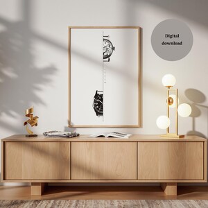 May include: A framed art print featuring a black and white illustration of two watch faces, one above the other, against a white background. The print is displayed above a wooden cabinet with a gold lamp and decorative items.