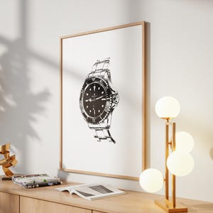 May include: A framed black and white illustration of a wristwatch. The watch has a round face with a rotating bezel and a metal band. The artwork is displayed on a white wall, with a wooden frame. A modern lamp with spherical lights is next to the artwork.