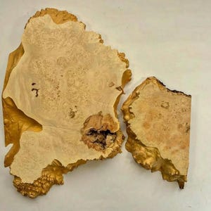 Könnte beinhalten: Zwei Stücke Holz in natürlicher, hellbrauner Farbe und einzigartiger, unregelmäßiger Form. Das Holz hat ein Maserungsmuster mit einer knorrigen Textur.