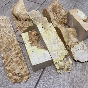 以下が含まれることがあります： ユニークな木目模様の明るい色の木片のコレクション。形や大きさが異なり、長方形に見えるものもあれば、より有機的なものもあります。木材は自然な質感の表面を持ち、木目の複雑なディテールを示しています。