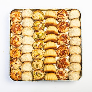 May include: A silver tray filled with a variety of small, round pastries. The pastries are arranged in rows and are a mix of light brown, tan, and white. Some of the pastries have nuts or seeds on top.