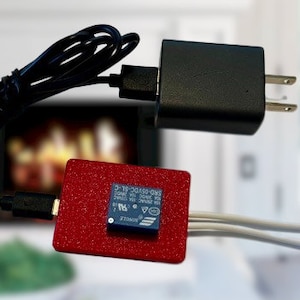 May include: A red circuit board with a small blue relay module attached to it. The relay module has the text "2-18-30152-01W" printed on it. A black USB power adapter is connected to the circuit board with a black cable. Two white wires with red wire caps are connected to the relay module.