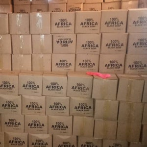 Puede incluir: Una pila de cajas de cart&oacute;n llenas de jab&oacute;n negro 100% Africa. Las cajas est&aacute;n apiladas en un almac&eacute;n o lugar de almacenamiento.