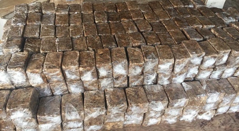 Puede incluir: Una gran pila de barras de jab&oacute;n rectangulares marrones envueltas en pl&aacute;stico transparente. Las barras est&aacute;n apiladas de forma ordenada y organizada.
