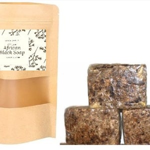Puede incluir: Tres barras de jab&oacute;n negro africano en una bolsa de papel marr&oacute;n. El jab&oacute;n es marr&oacute;n oscuro y tiene una textura rugosa. La bolsa tiene una etiqueta que dice "100% Jab&oacute;n Negro Africano Puro".