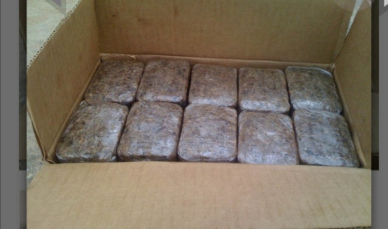 Puede incluir: Una caja de cart&oacute;n llena de 12 barras rectangulares marrones envueltas en pl&aacute;stico transparente.