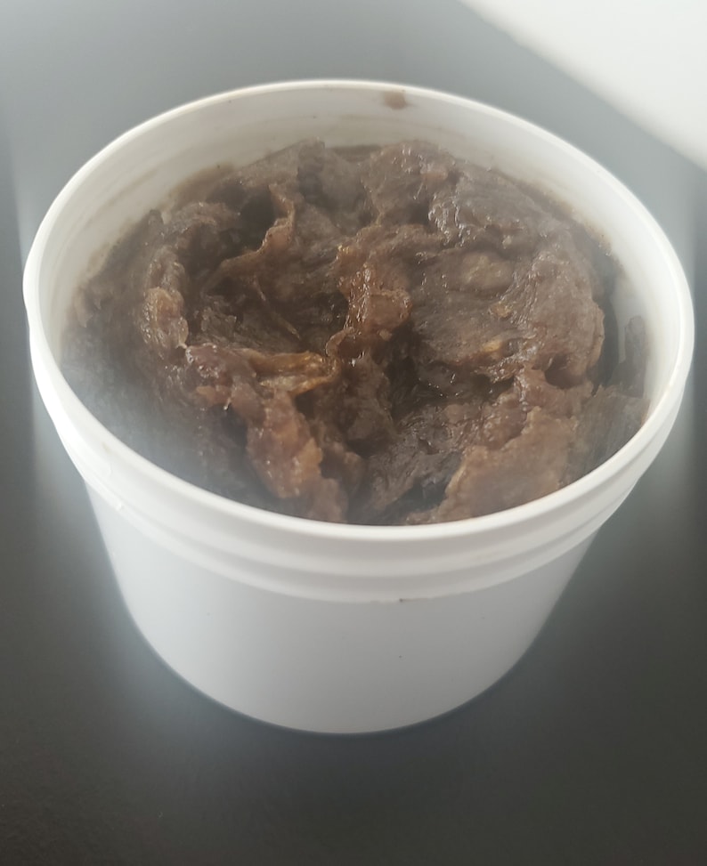 Puede incluir: Un recipiente de pl&aacute;stico blanco lleno de una sustancia espesa y texturizada de color marr&oacute;n oscuro. La sustancia parece ser un exfoliante corporal o jab&oacute;n hecho en casa.