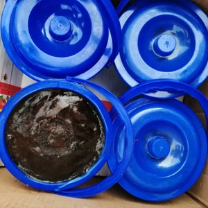 Puede incluir: Cuatro contenedores de pl&aacute;stico azul con tapas. Un contenedor est&aacute; abierto y lleno de una sustancia marr&oacute;n oscura.