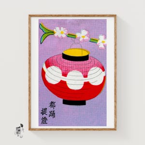 Puede incluir: Impresión enmarcada de una ilustración de linterna japonesa. La linterna roja y blanca está suspendida de una rama con flores rosas y blancas. El fondo es de color púrpura claro, con texto japonés en el lado izquierdo.